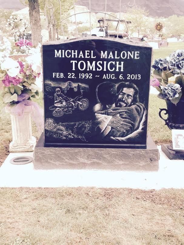 Grave of Michael Malone Tomsich: black headstone with engraved pictures, flowers, and dates.
