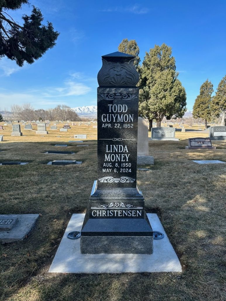 Gravestone in a cemetery with names Todd Glynok and Linda Money against a mountain backdrop.