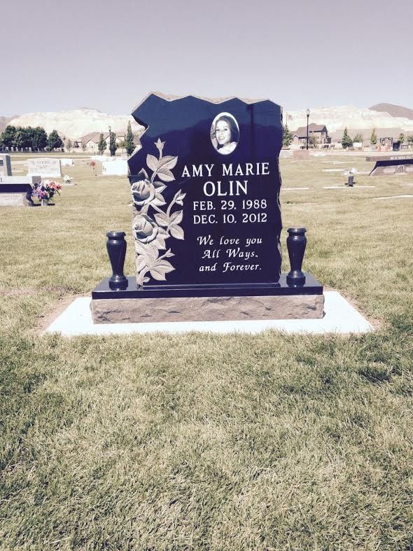 Gravestone of Amy Marie Olin, black with a photo, flowers, and inscription; set in a cemetery.