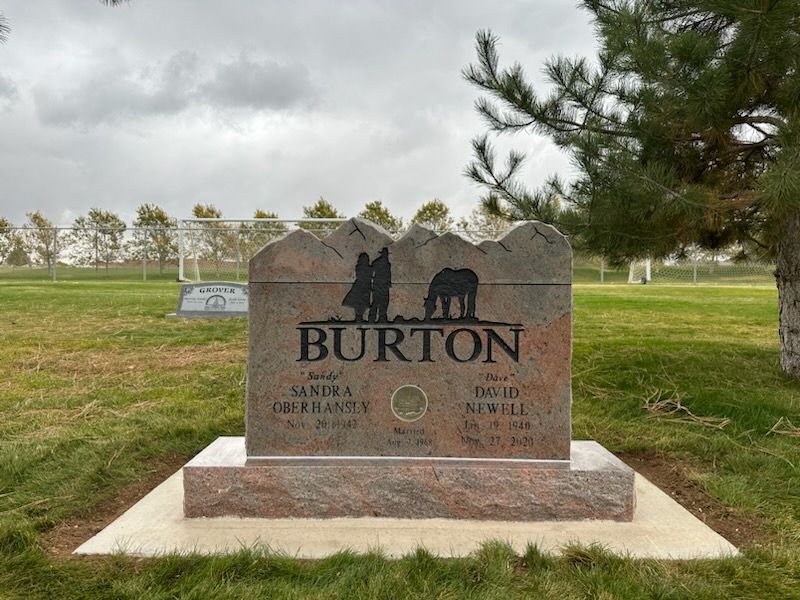 Gravestone for the Burton family. Brown stone with a mountain design and silhouette of people with a horse.
