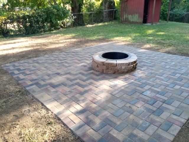 Paver patio with a brick fire pit in a yard.