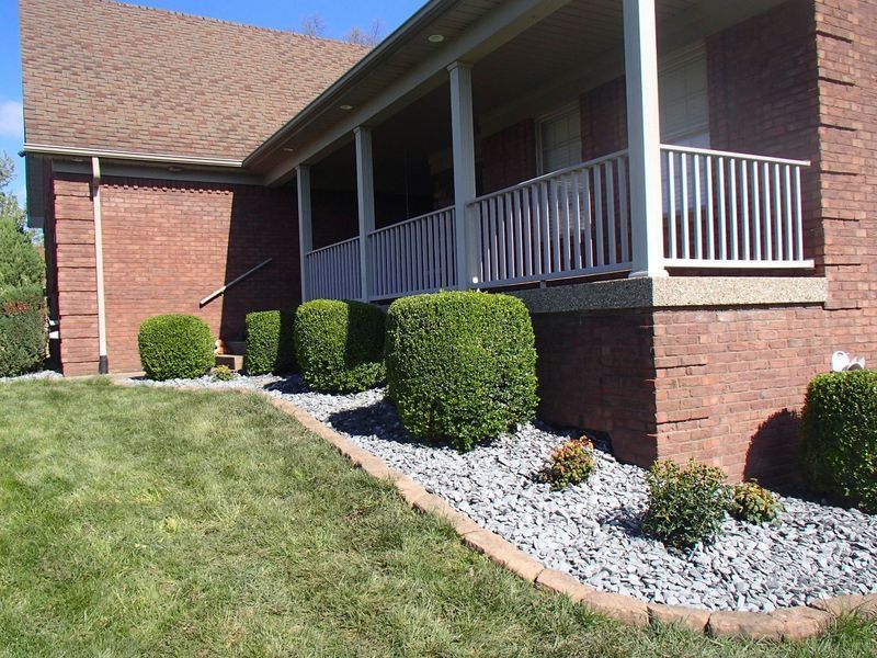 Red brick house with a porch and manicured bushes in a rock garden.
