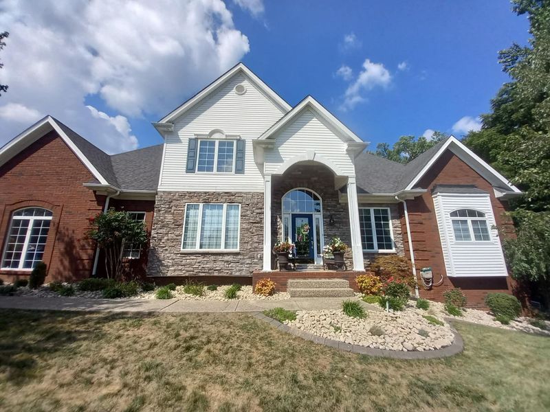 Brick house with stone facade, white trim, and blue shutters under a blue sky.