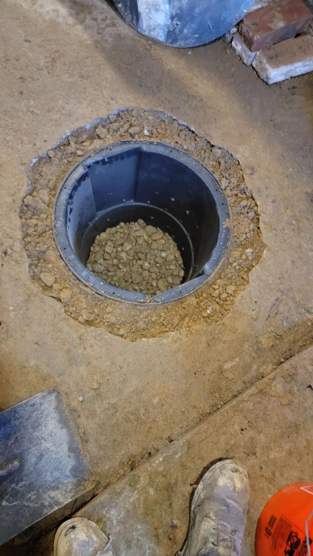 A person is standing next to a hole in the ground with gravel in it.