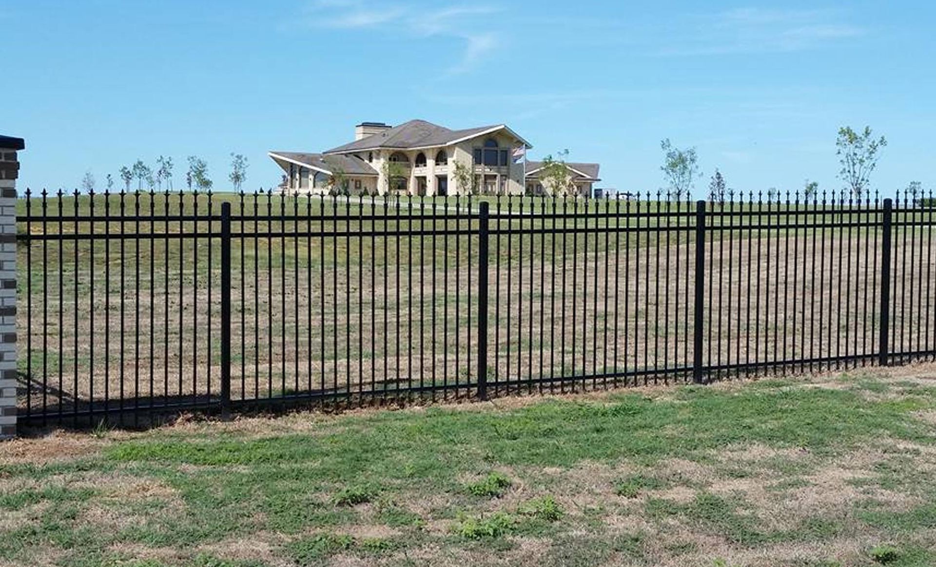 A large house is behind a black metal fence.