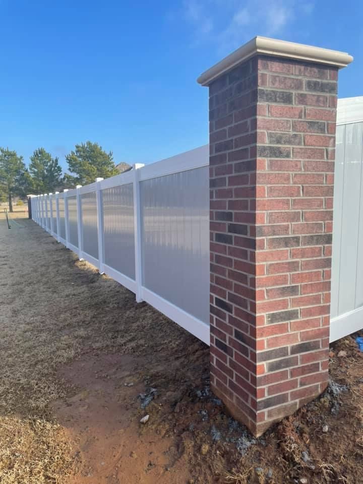 A white fence with a red brick post in front of it.