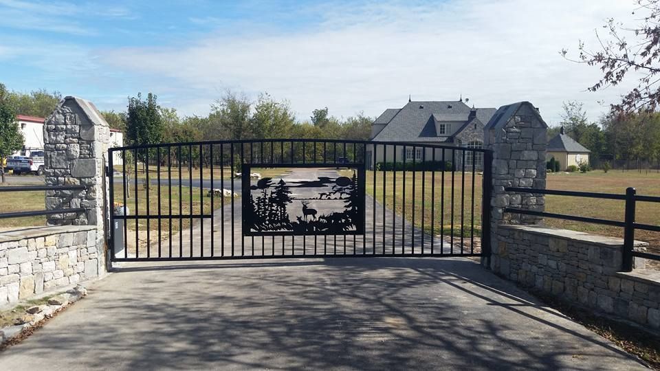 A black gate with a picture on it is leading to a house.