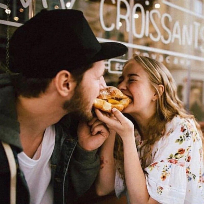 A man and a woman are eating croissants in front of a croissant shop.