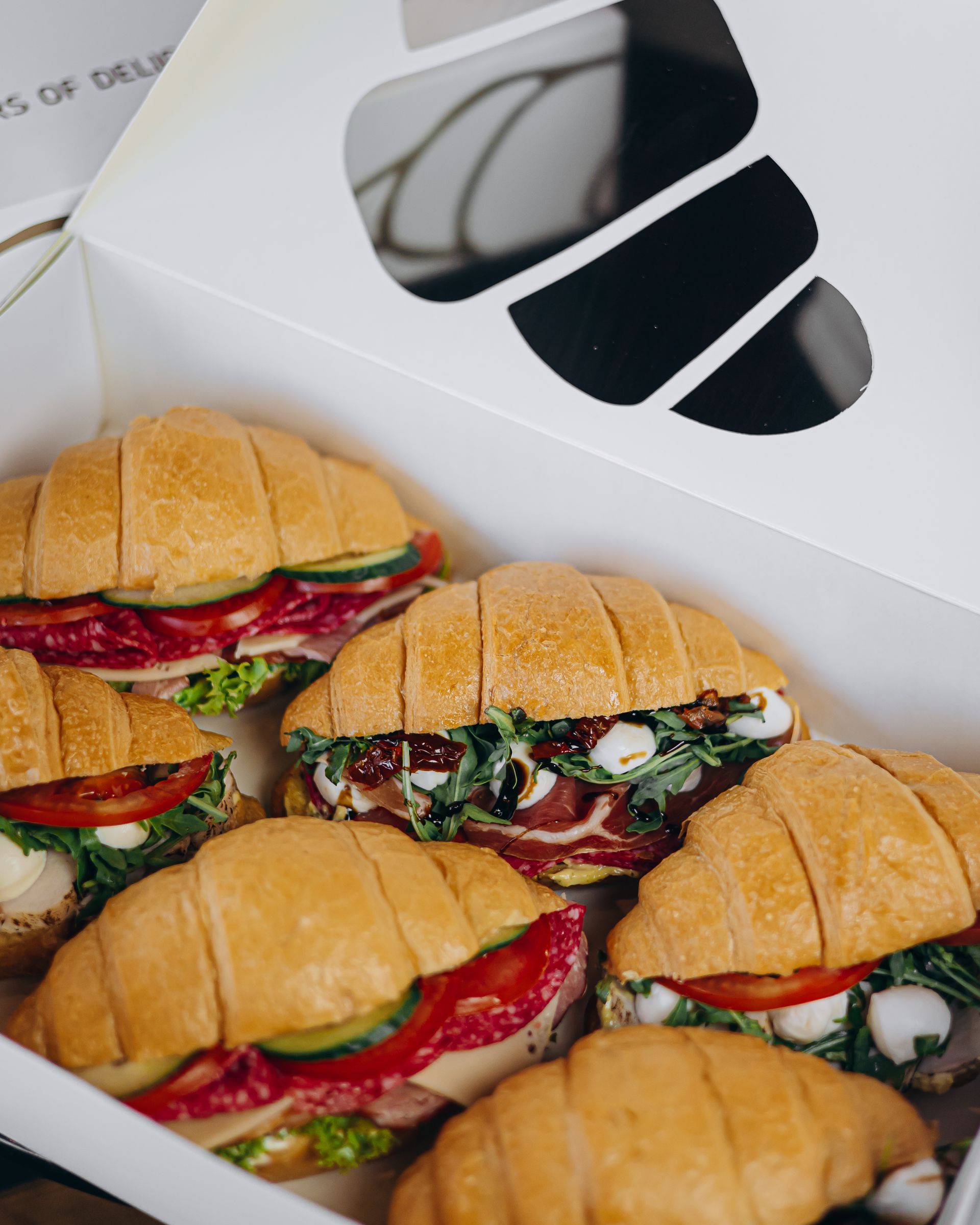 Box of croissant sandwiches, filled with various ingredients, ready for delivery.