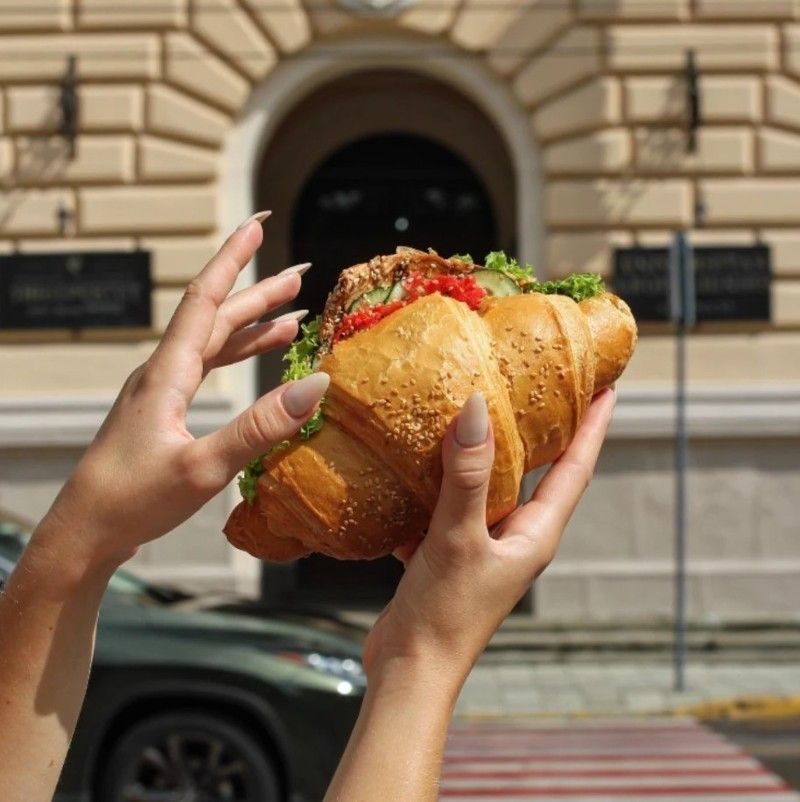 A person is holding a croissant with a sandwich on it.