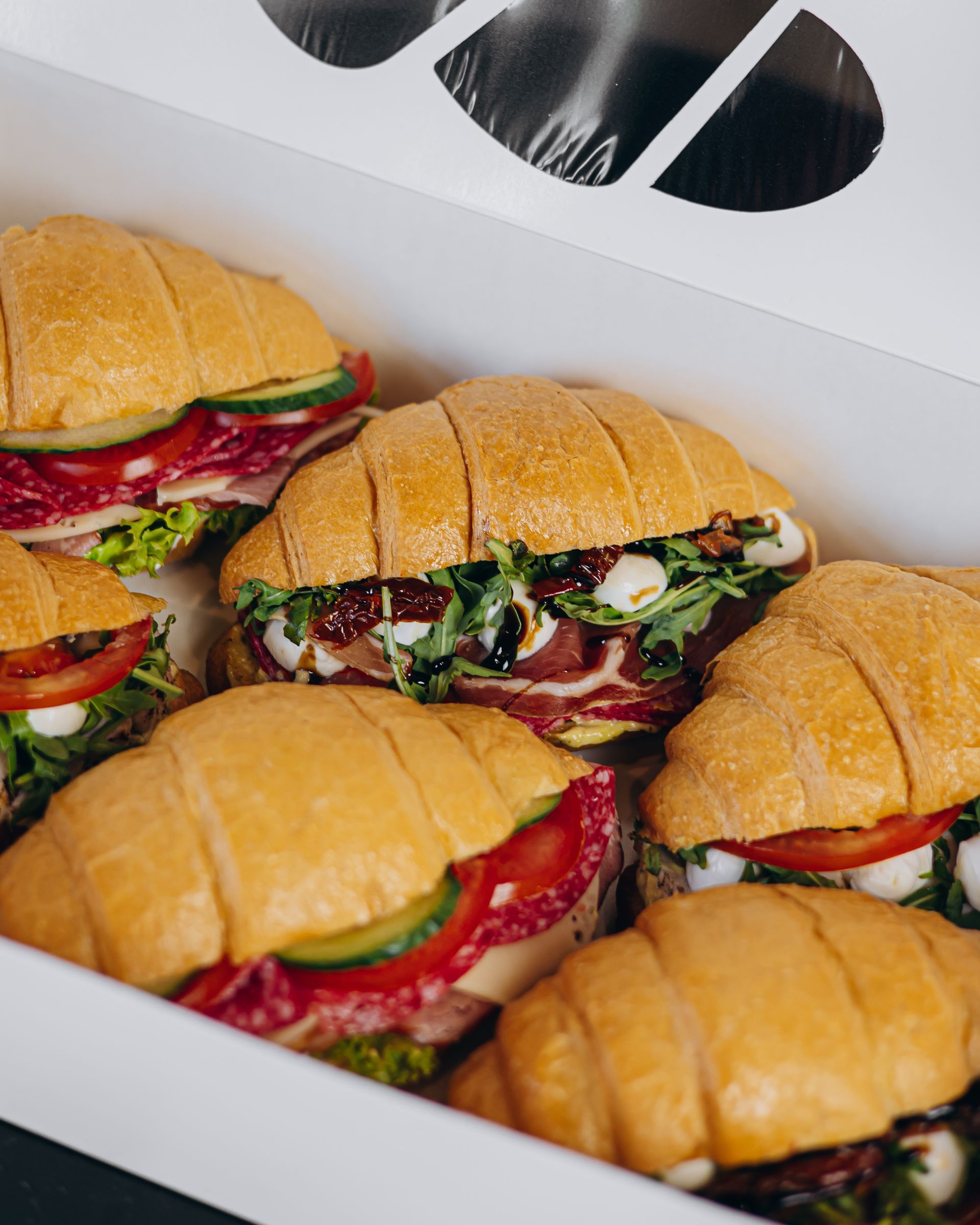 Box of assorted croissant sandwiches with various fillings.