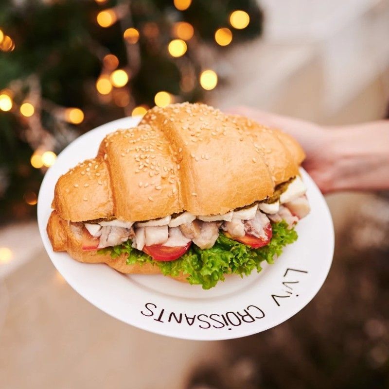 A person is holding a plate with a sandwich on it that says liv croissants.