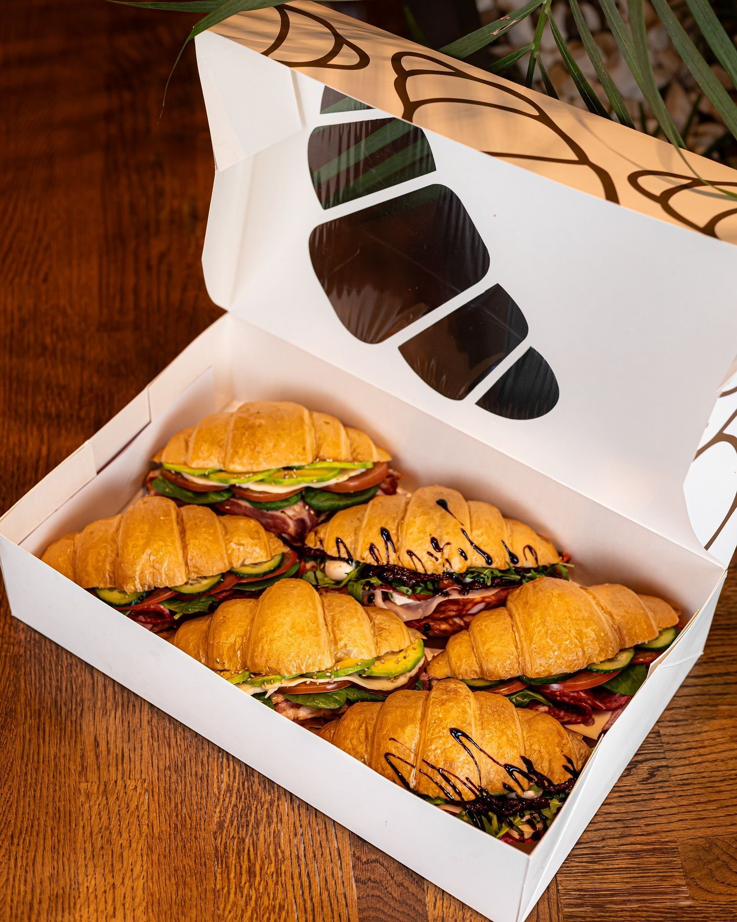 A box filled with croissant sandwiches on a wooden table.