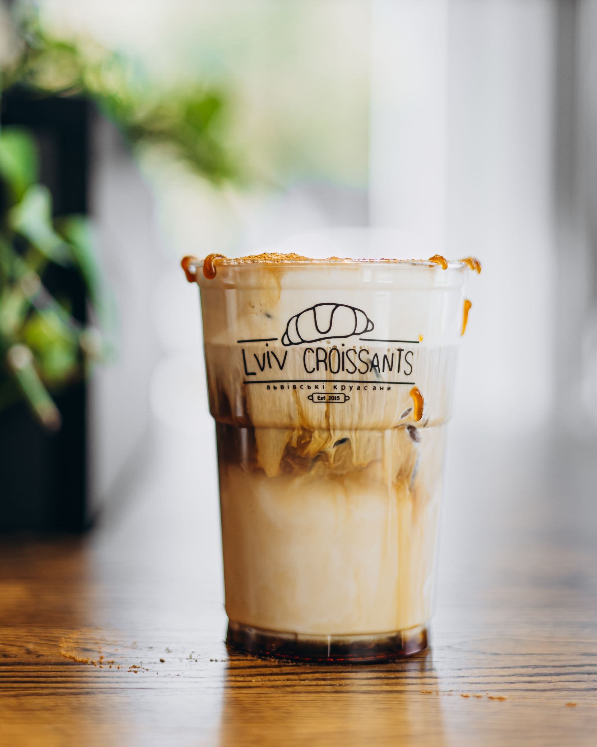 Iced coffee in a plastic cup with a caramel rim, on a wooden table.