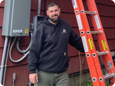 Electrician in orange and black gloves, wiring a light switch in a wall. Tools and blueprints are nearby.