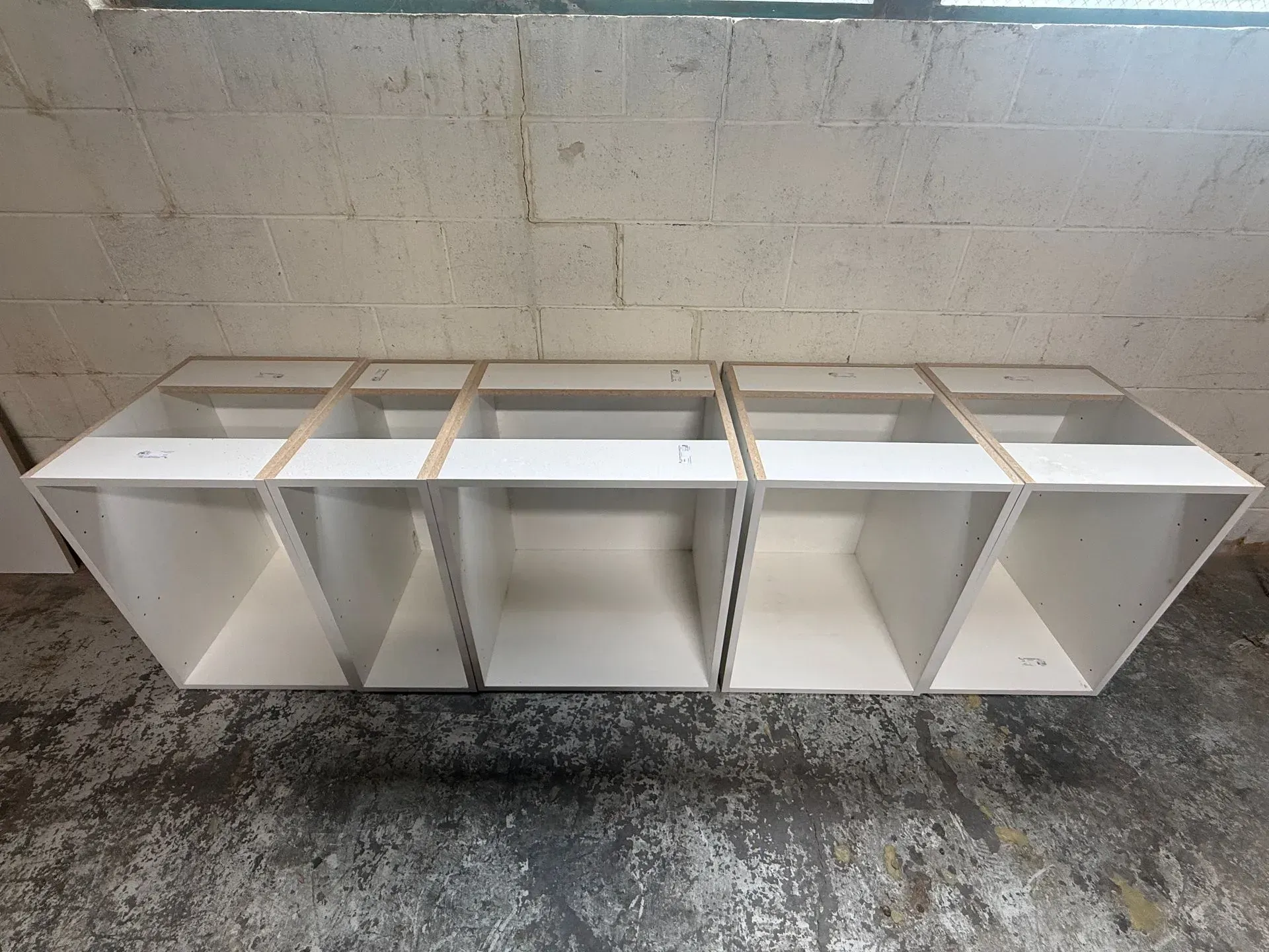 White modular shelving unit against a tiled wall in a bathroom or utility area, with open cubby sections.