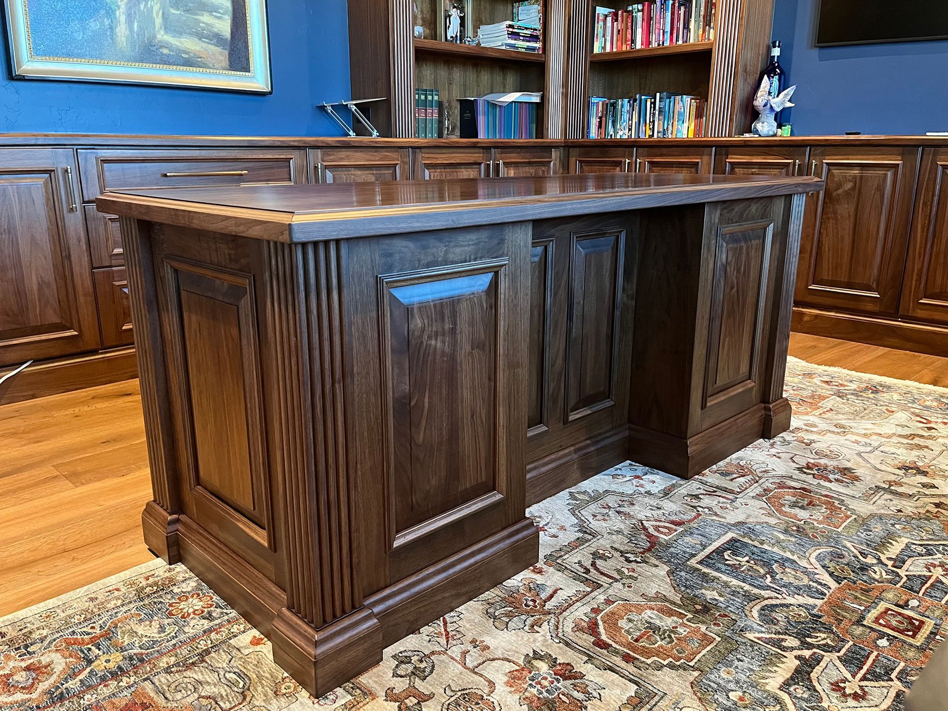 Dark wood executive desk in a room with blue walls and a patterned rug.