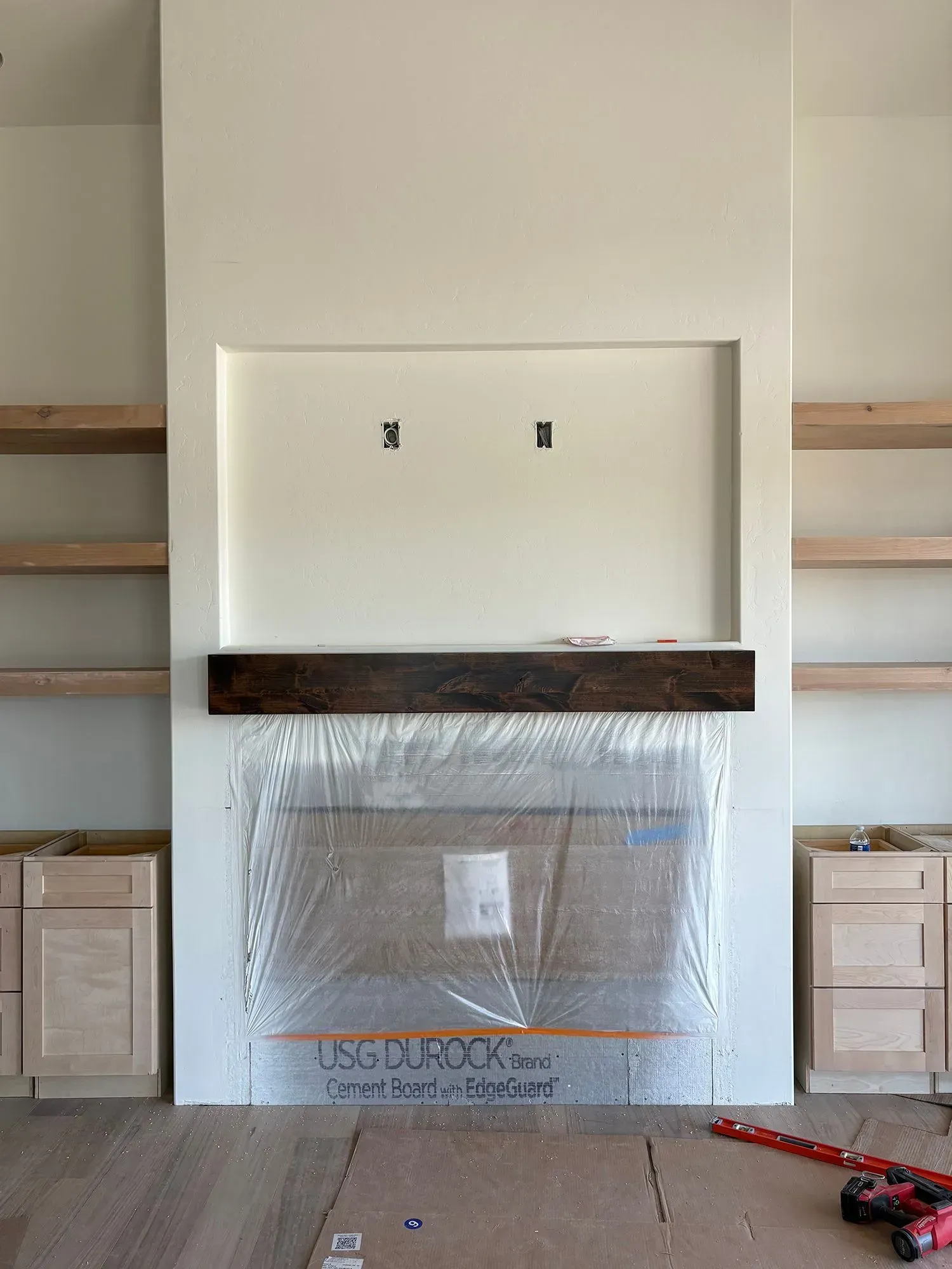 Empty living room wall with a centered white fireplace and wooden mantel, partially covered in protective plastic.