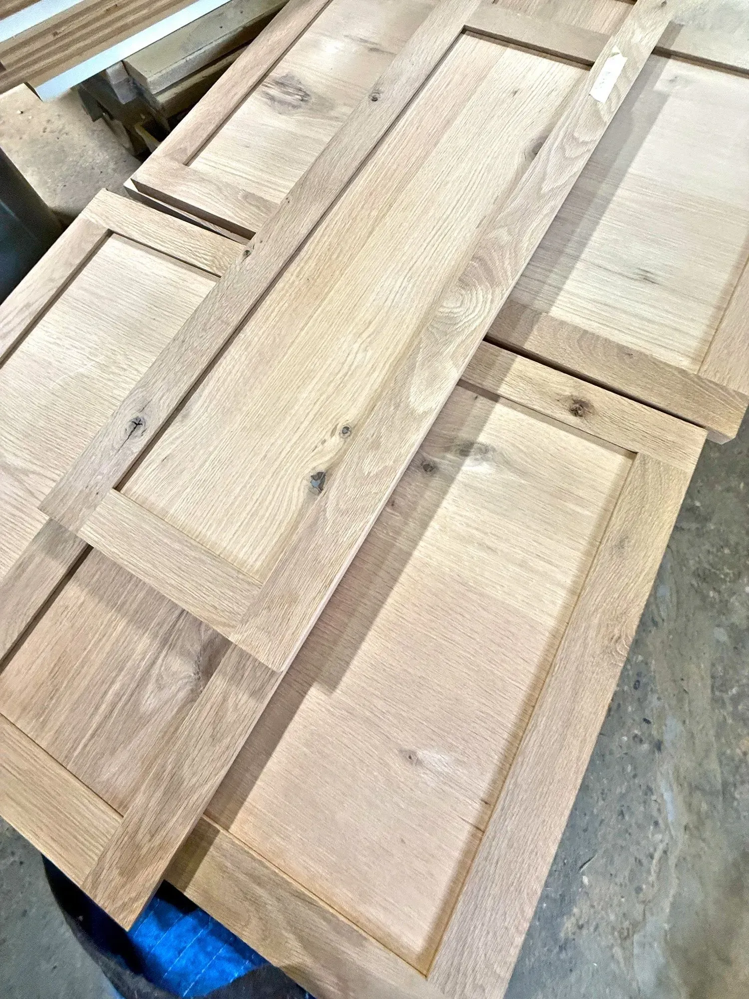 Stacked unfinished wooden cabinet doors on a workshop floor, light tan with inset panels.