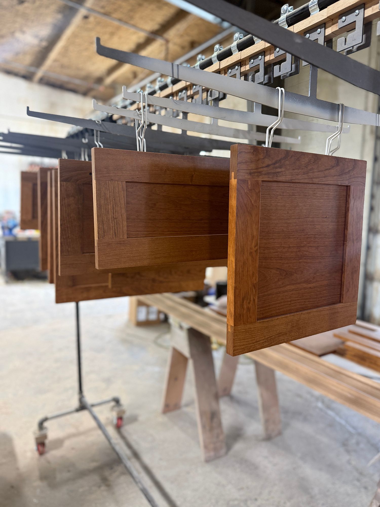 Wooden cabinet doors hanging on a spray rack in a workshop, with wet stain or finish drying