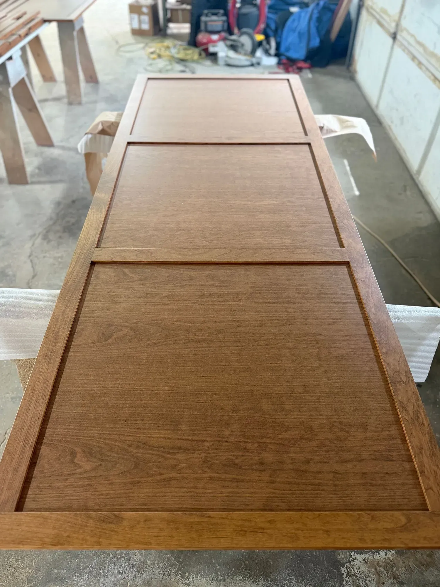 Three-panel wooden cabinet door lying on a workshop table, with recessed rectangular panels.