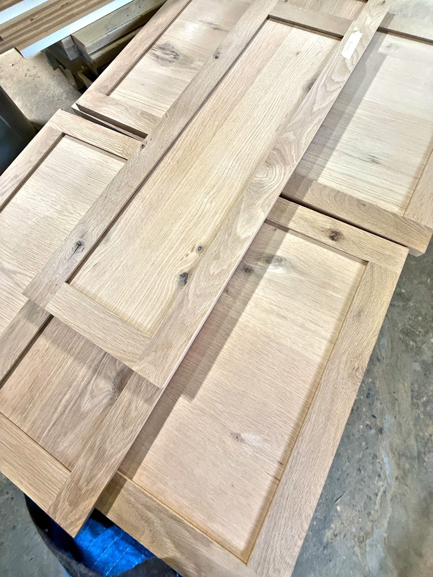 Stack of unfinished light wood cabinet doors with recessed panels in a workshop.