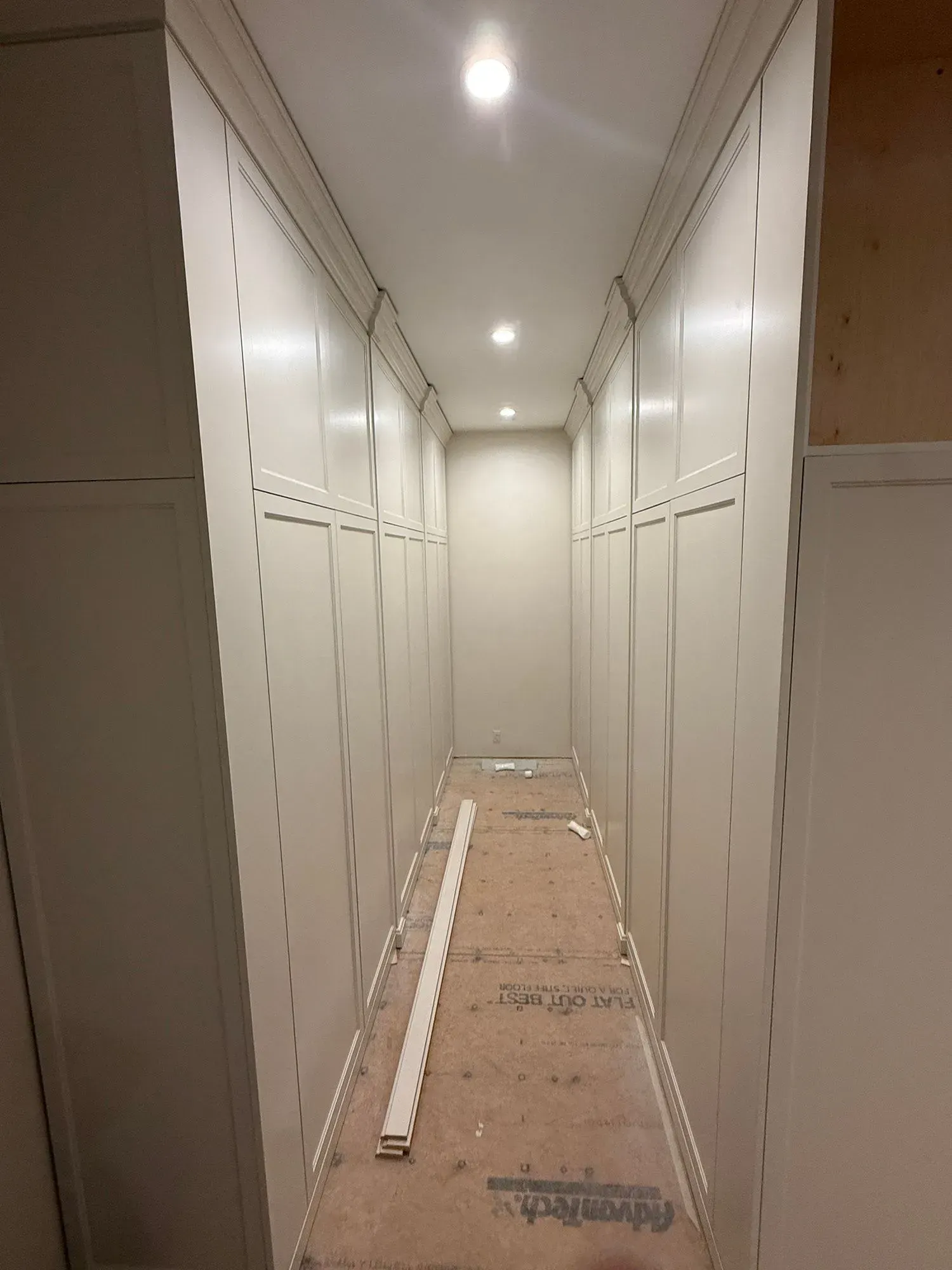 Narrow hallway with white cabinets and a protective floor covering under construction.