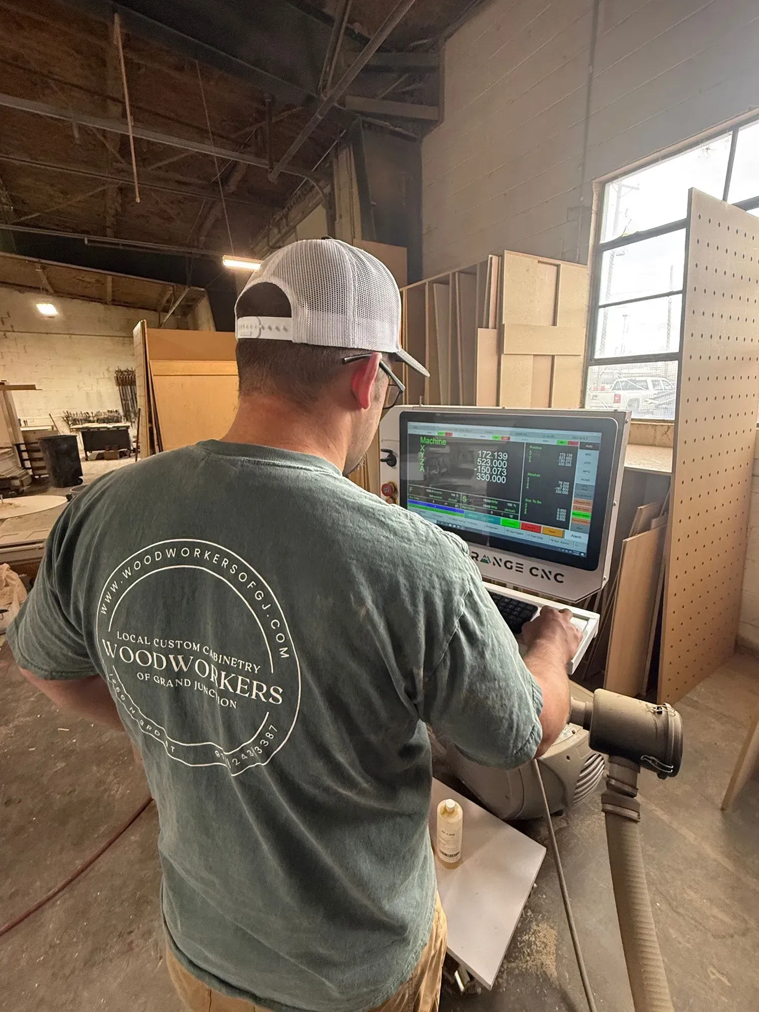 Worker in a warehouse operating a touchscreen control panel beside stacked cardboard boxes.
