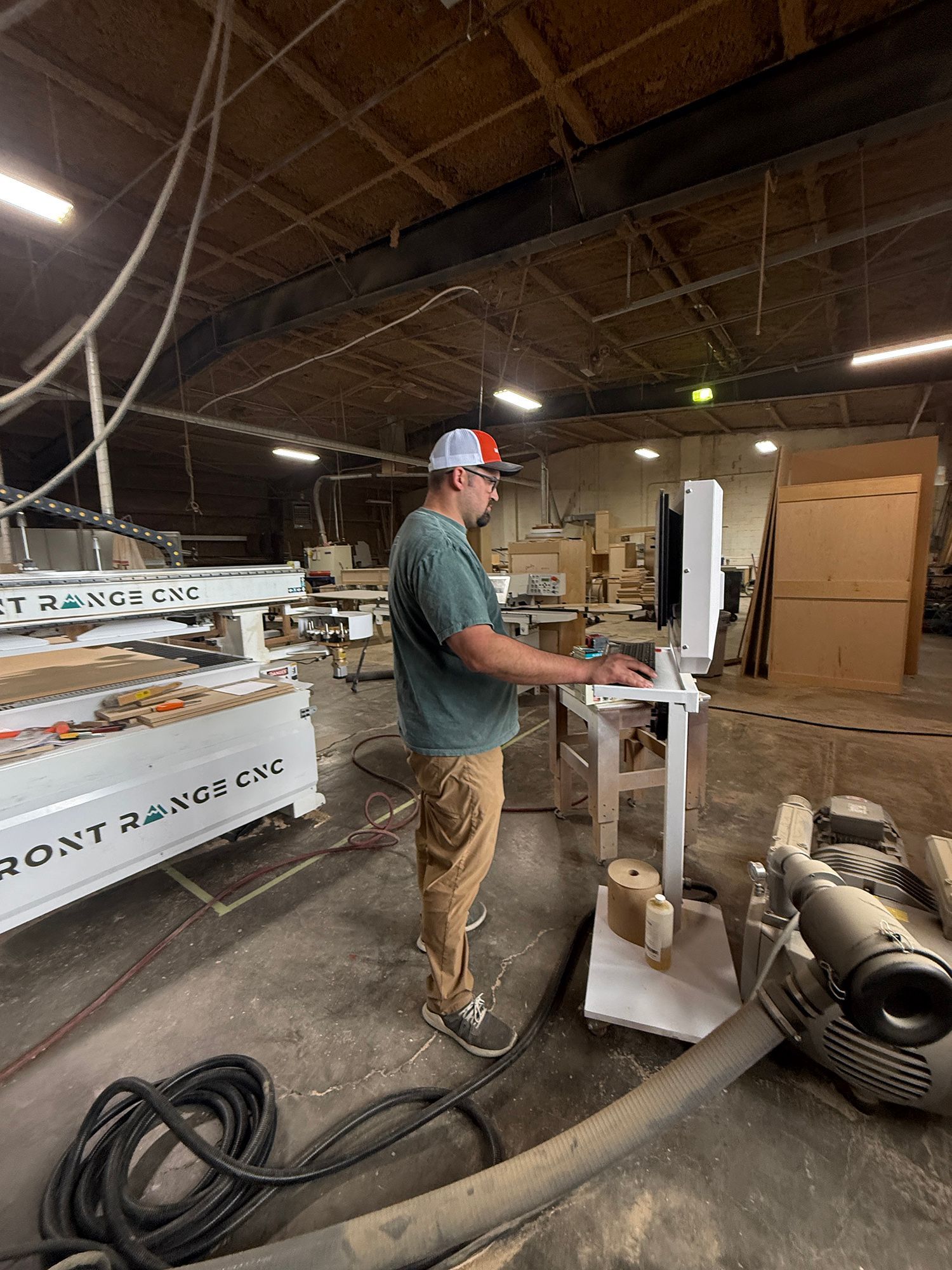 Worker in hard hat operating a machine in a workshop with lumber and industrial equipment.