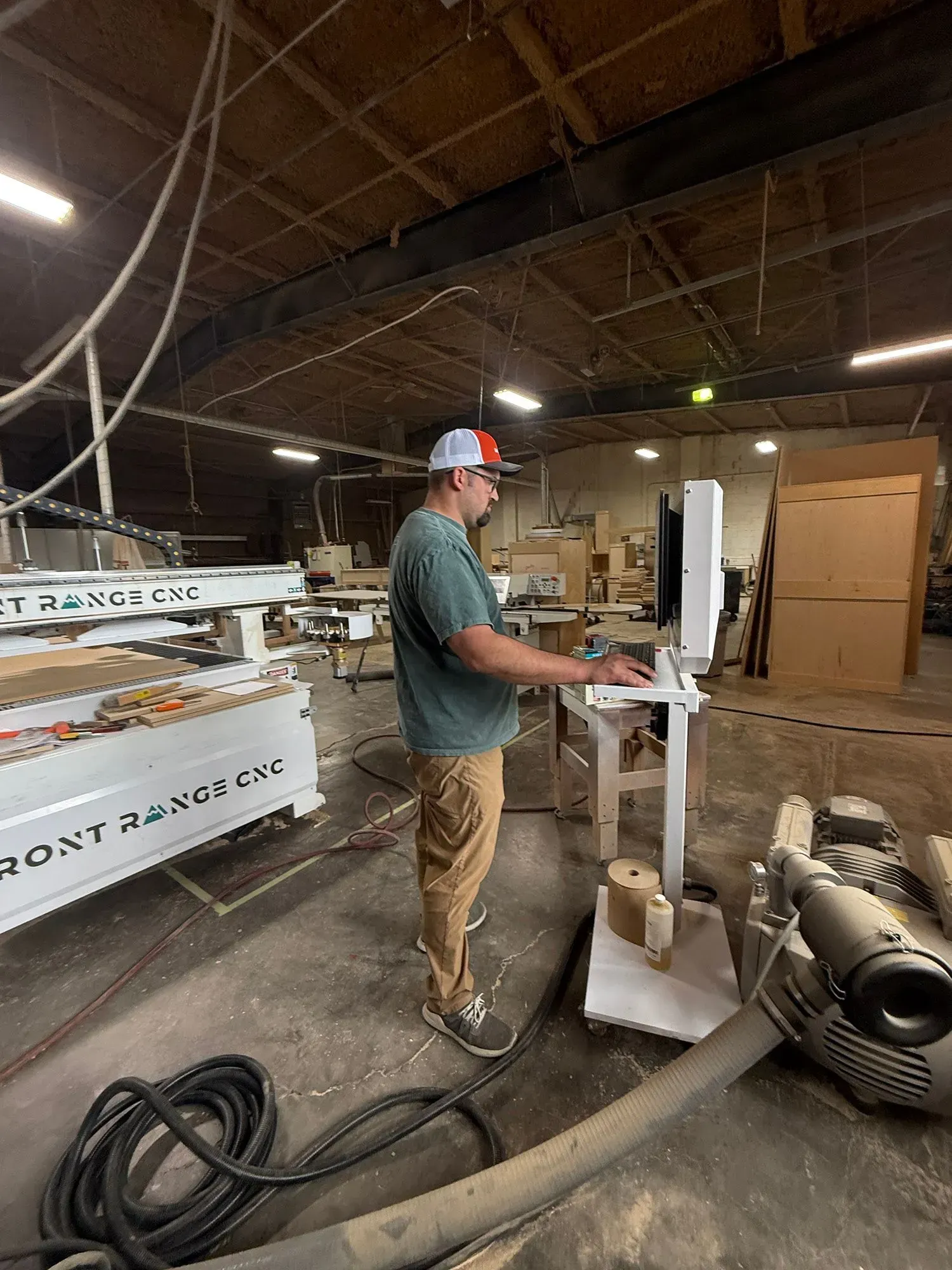 Worker sanding a large white panel in an industrial workshop, with tools and equipment nearby.