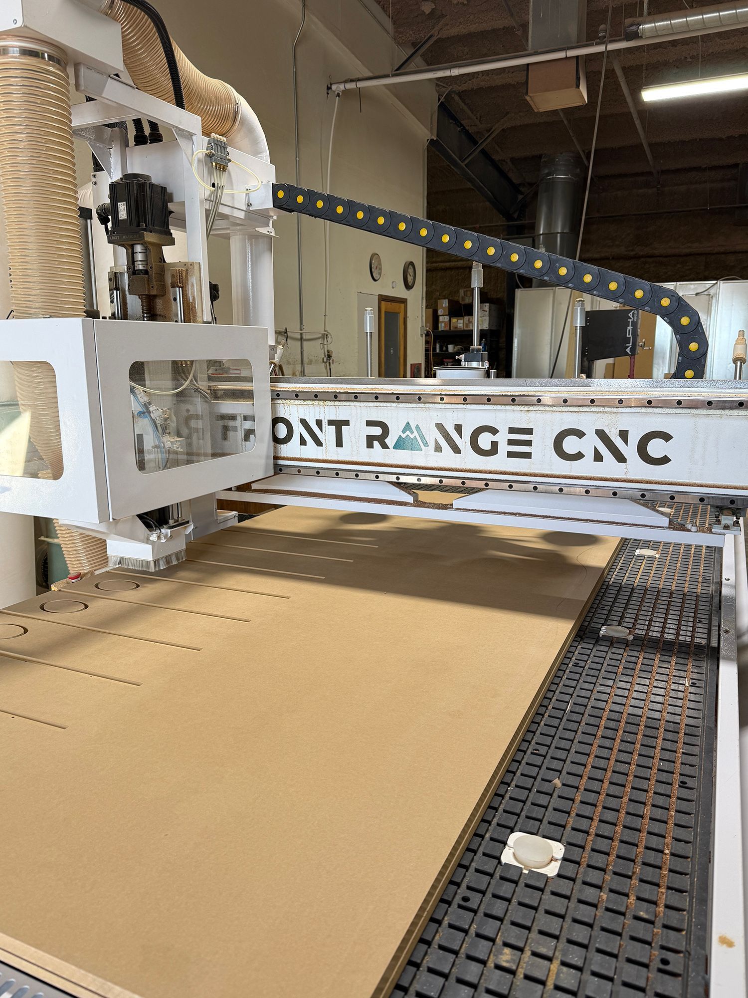 CNC machine cutting a large cardboard sheet in a workshop, with a moving gantry and conveyor bed