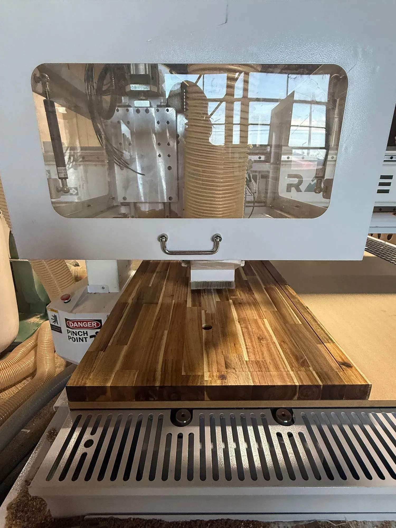 Close-up of a white machine with windowed front over a wooden worktable in a workshop.