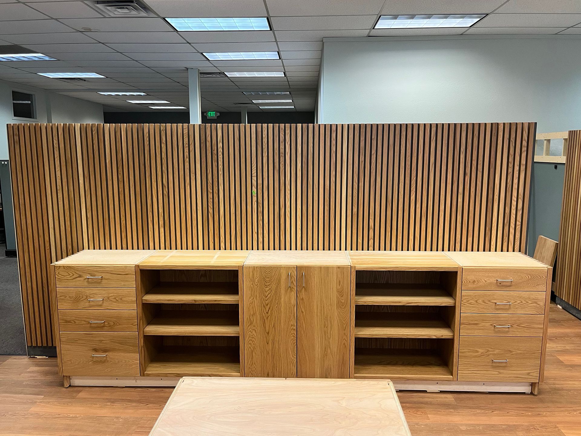 Wooden media console with shelves and drawers against a slatted wood divider in an office lobby