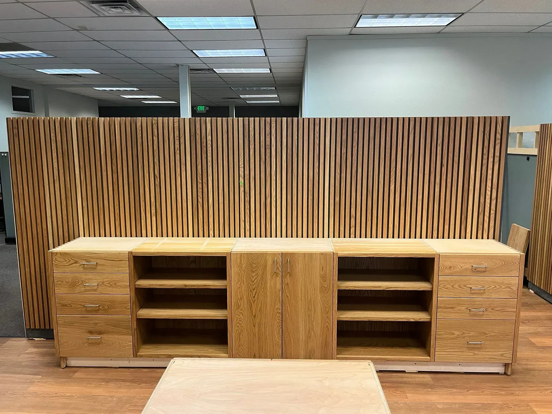 Wooden office storage cabinets against a slatted wood wall in a commercial interior.