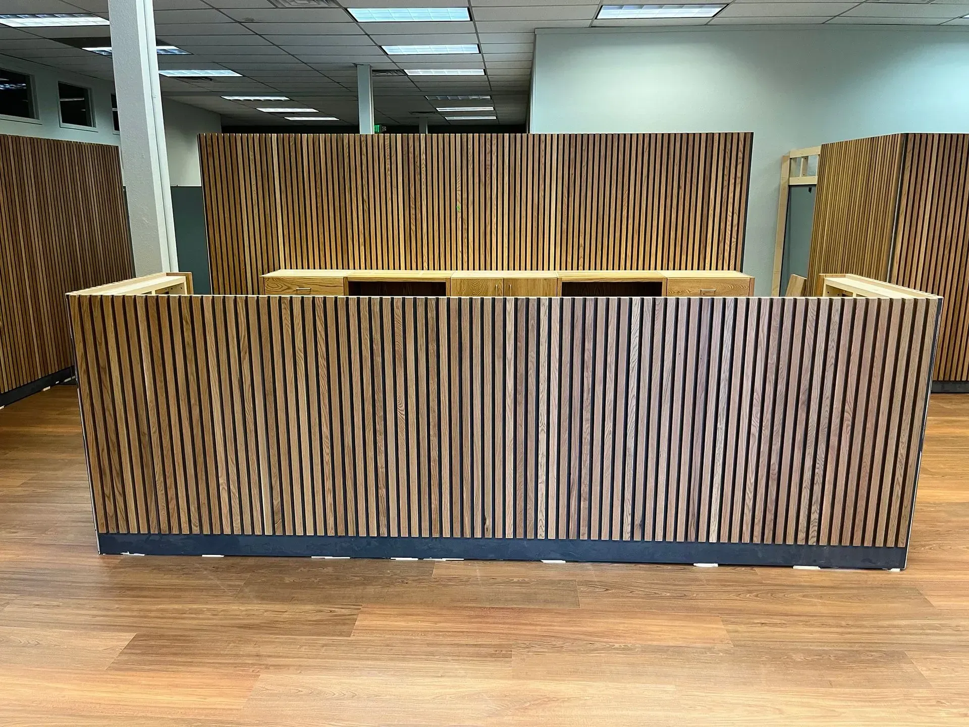Wood-paneled reception desk in a modern office lobby with wood flooring and ceiling lights.