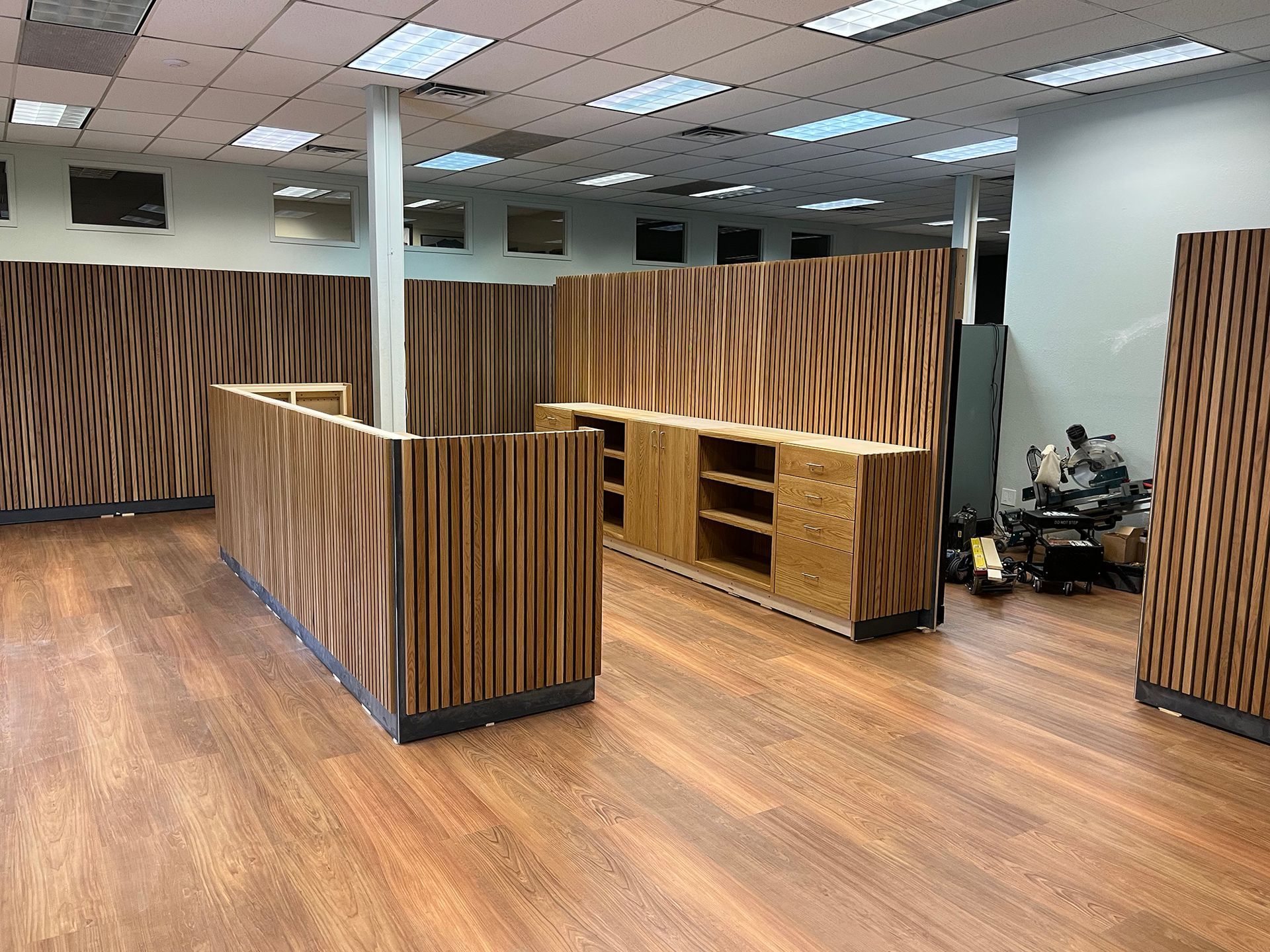 Empty office lobby with wood-paneled counters, wood floor, and a person sitting in the corner