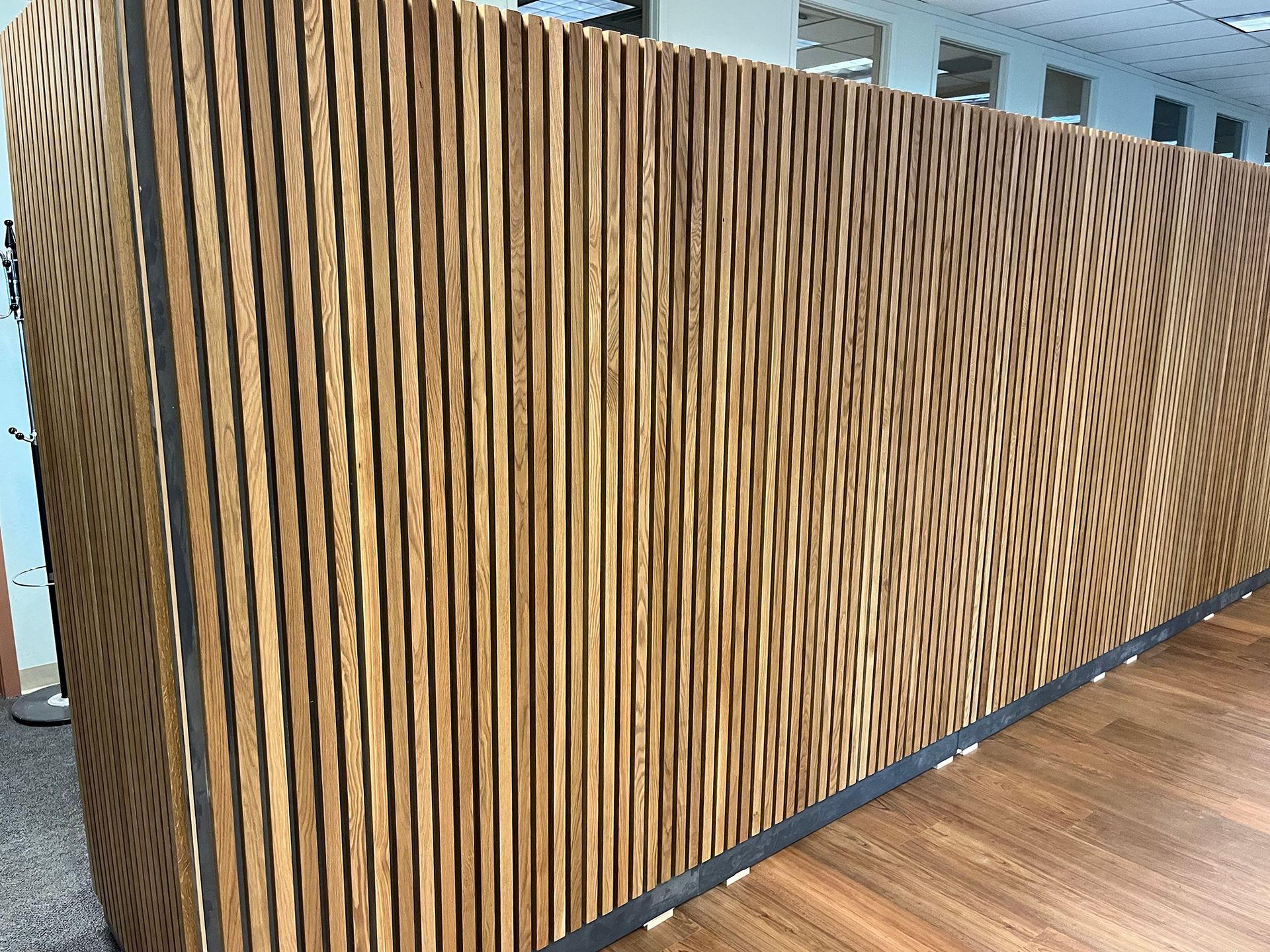 Wooden slatted wall with flowing wood grain beside a polished wood floor in a modern interior