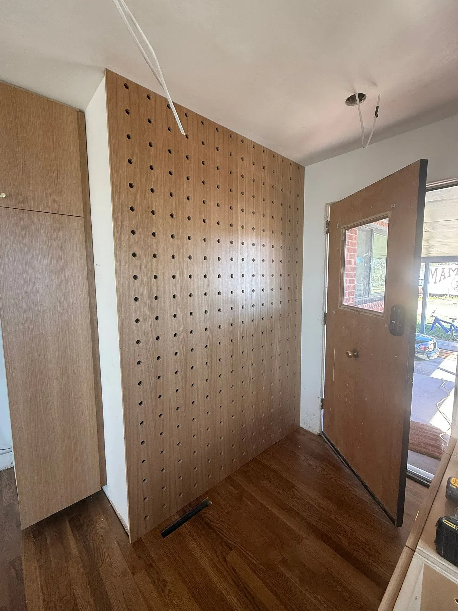 Interior room with a pegboard wall, wood floor, and an open door to outside.