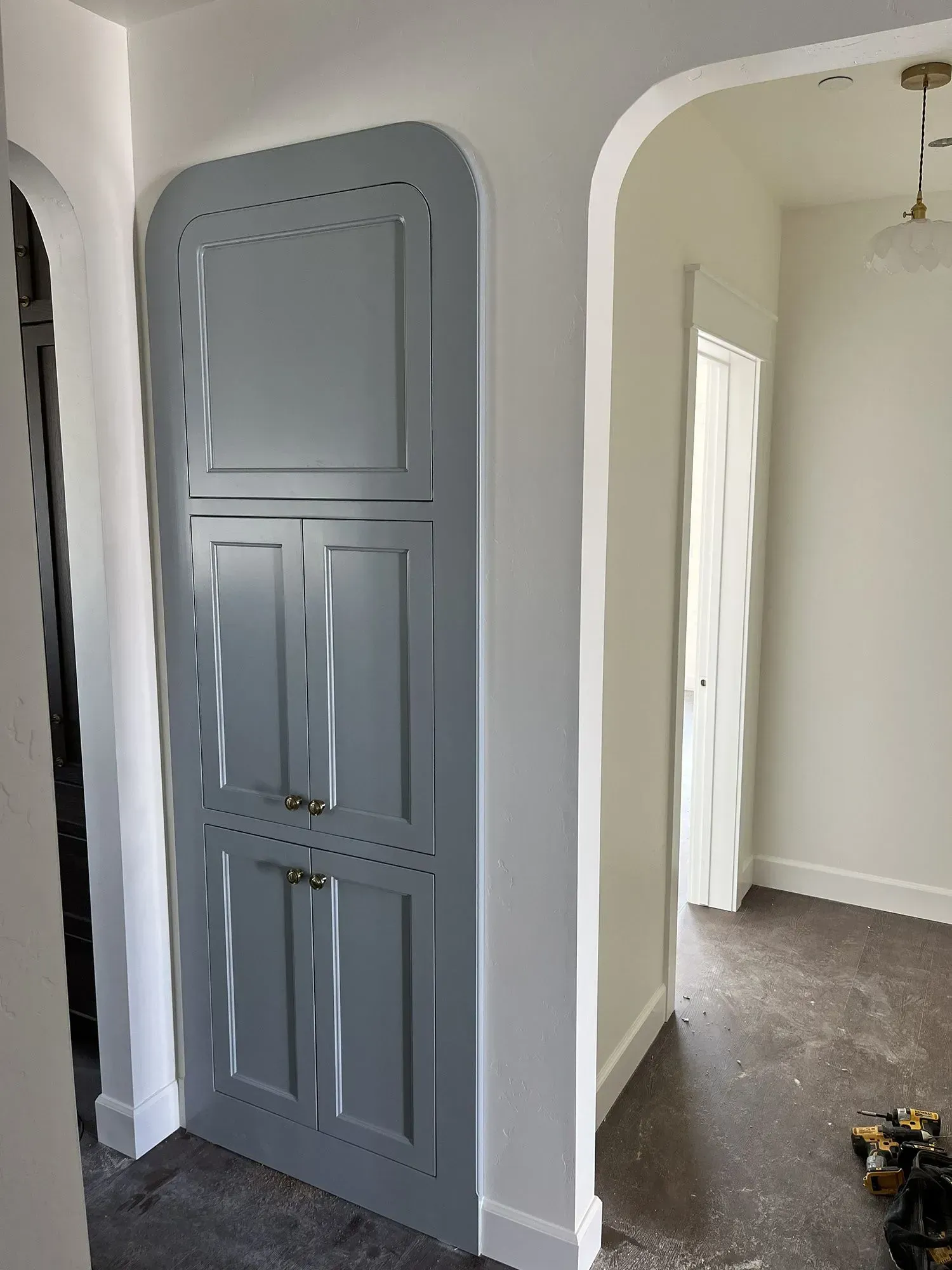 Gray built-in wall cabinet in a white hallway leading to an empty room with dark floors.