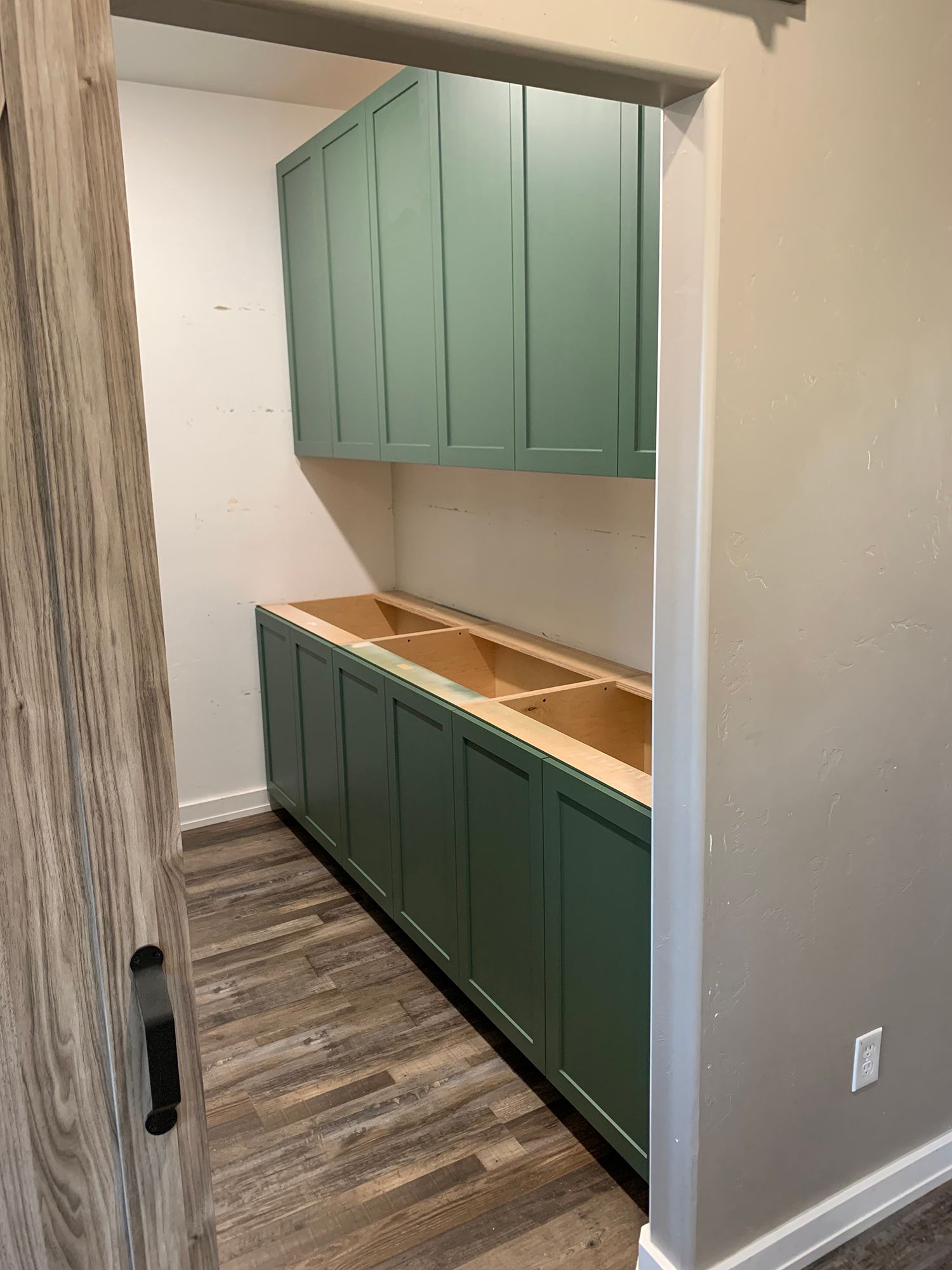 Narrow hallway with sage green built-in cabinets and open countertop under a pass-through opening