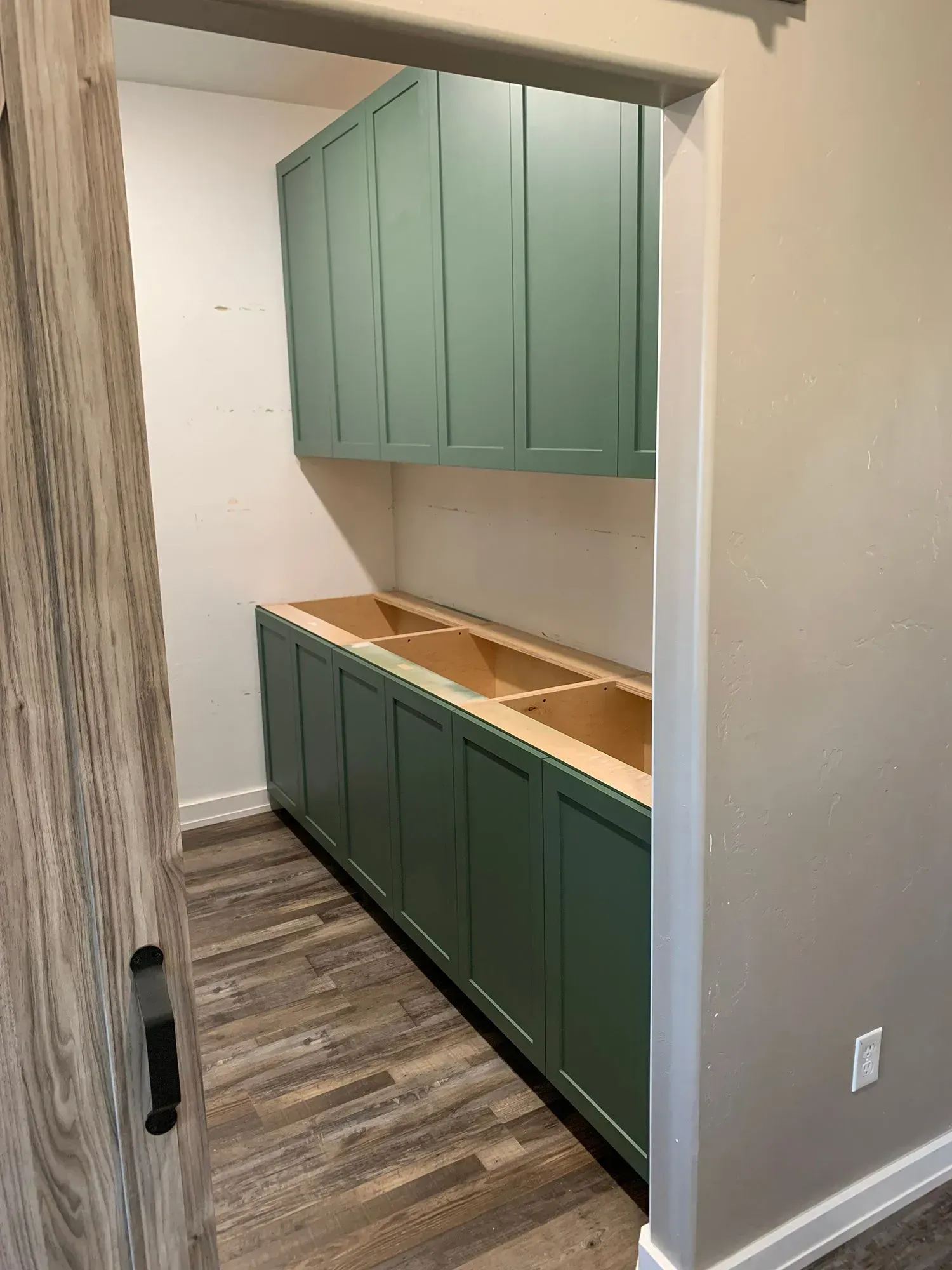 Green cabinets and open wood countertop in a narrow hallway nook with wood-look flooring.