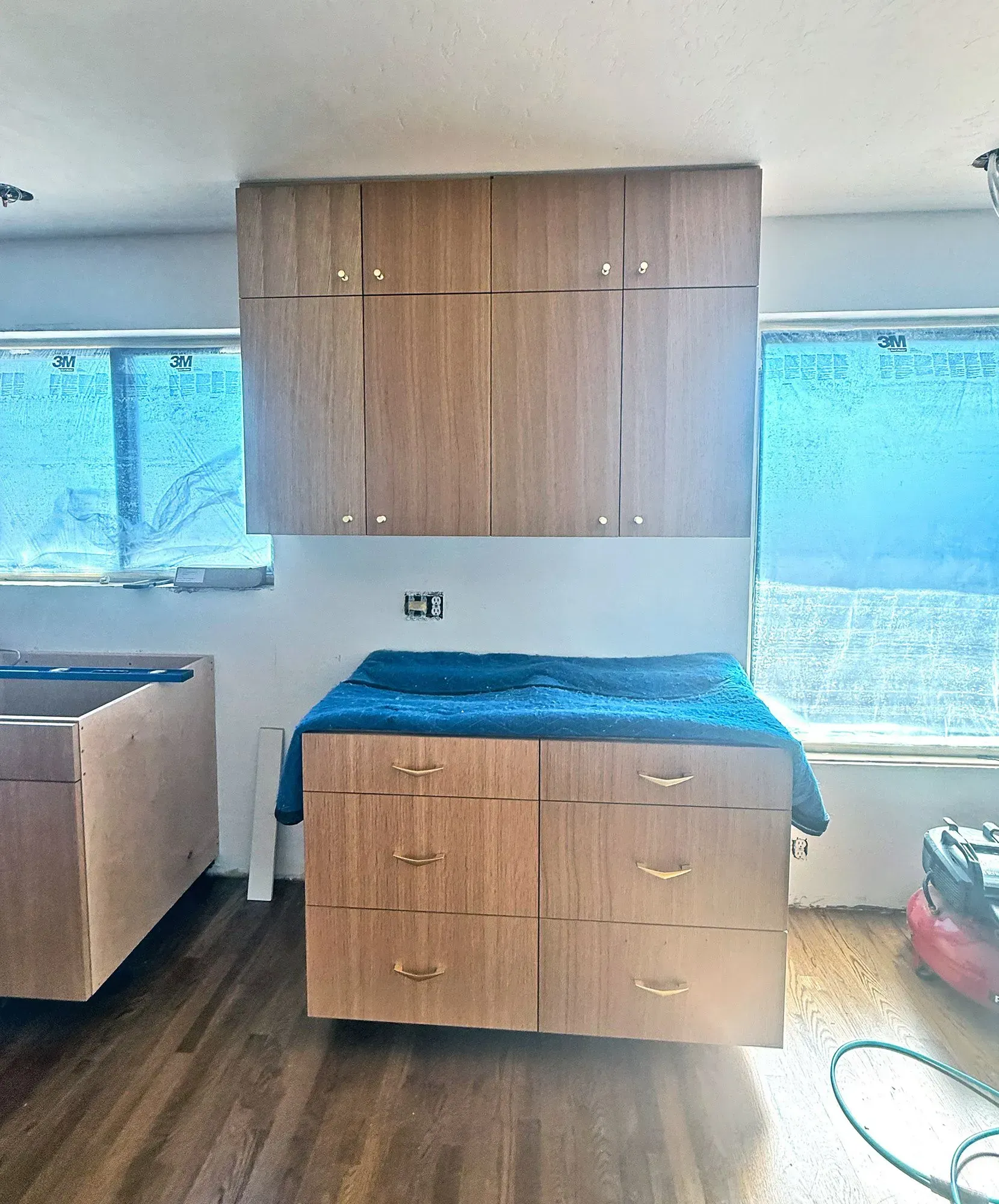 Wood-paneled cabinetry and drawers in a bright room, with a blue-covered counter beneath a wall cabinet.
