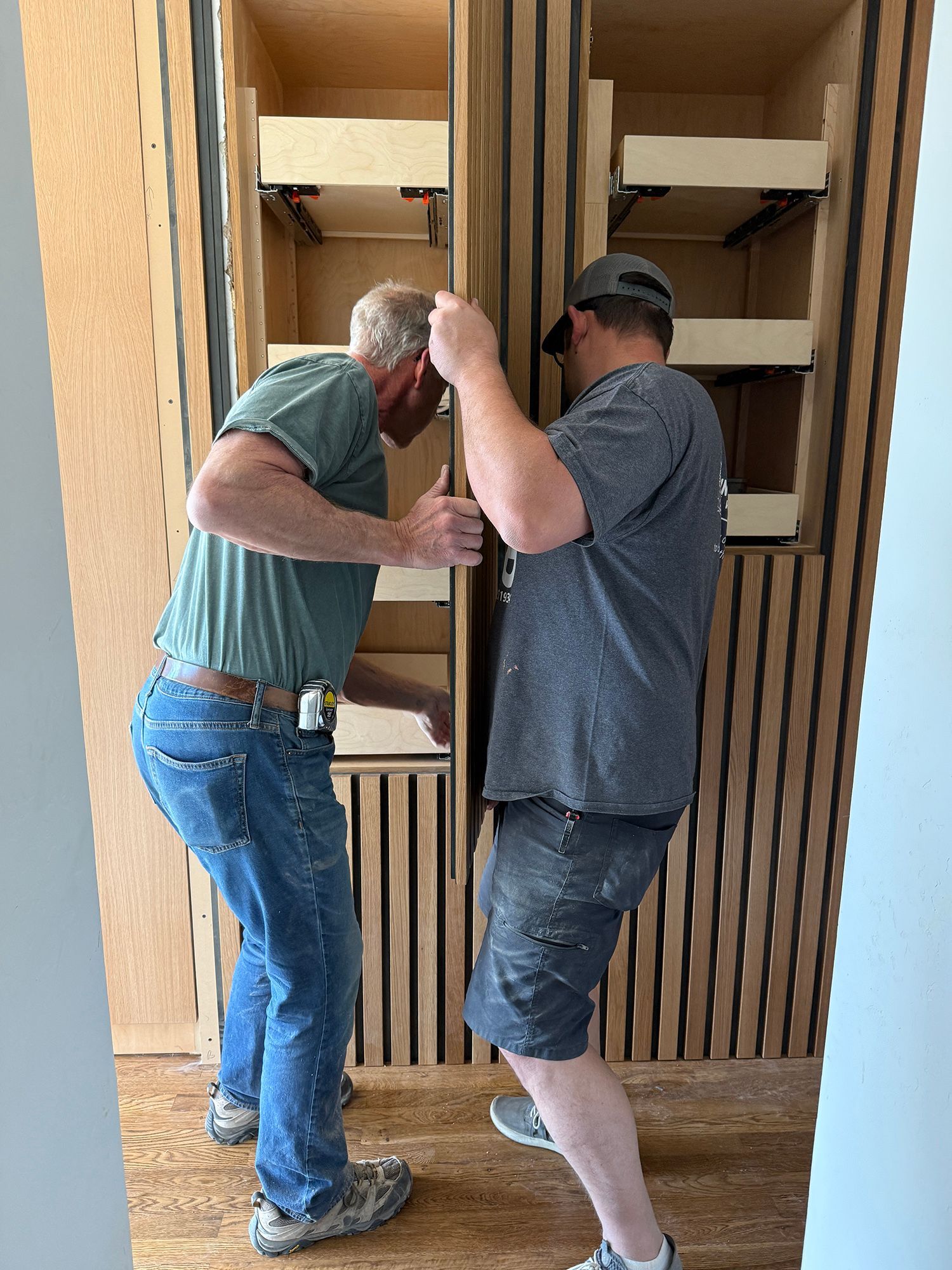 Two men working together to install wooden shelving in a closet nook.