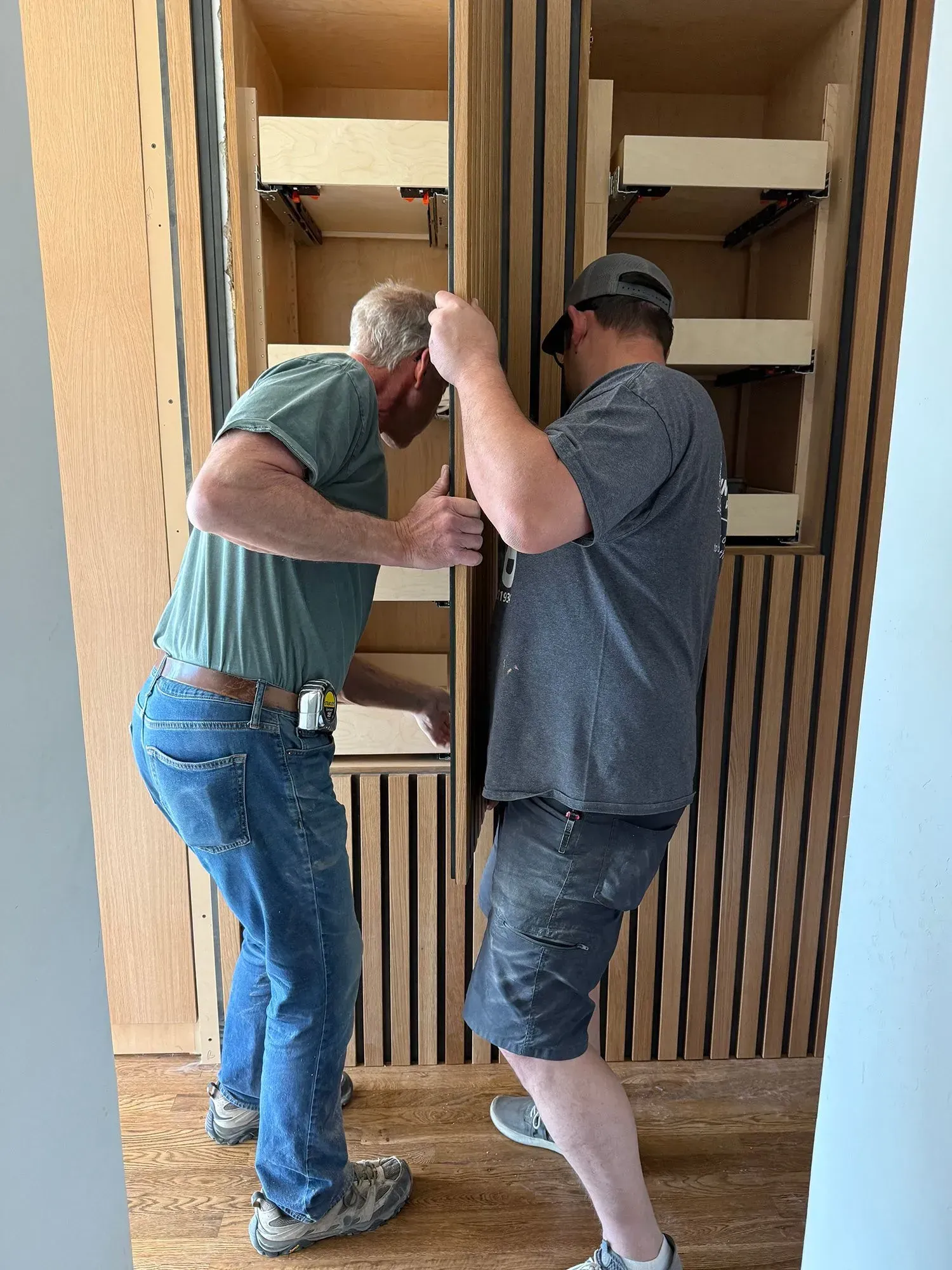 Two men moving a large wooden cabinet through a doorway indoors.