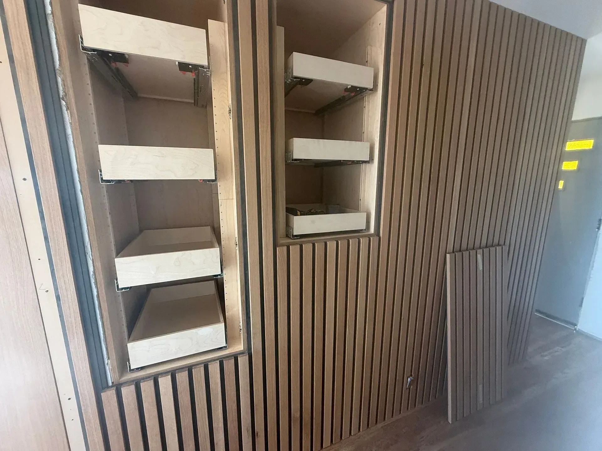 Wood-paneled wall with recessed shelves and a small grille in a modern interior corridor.