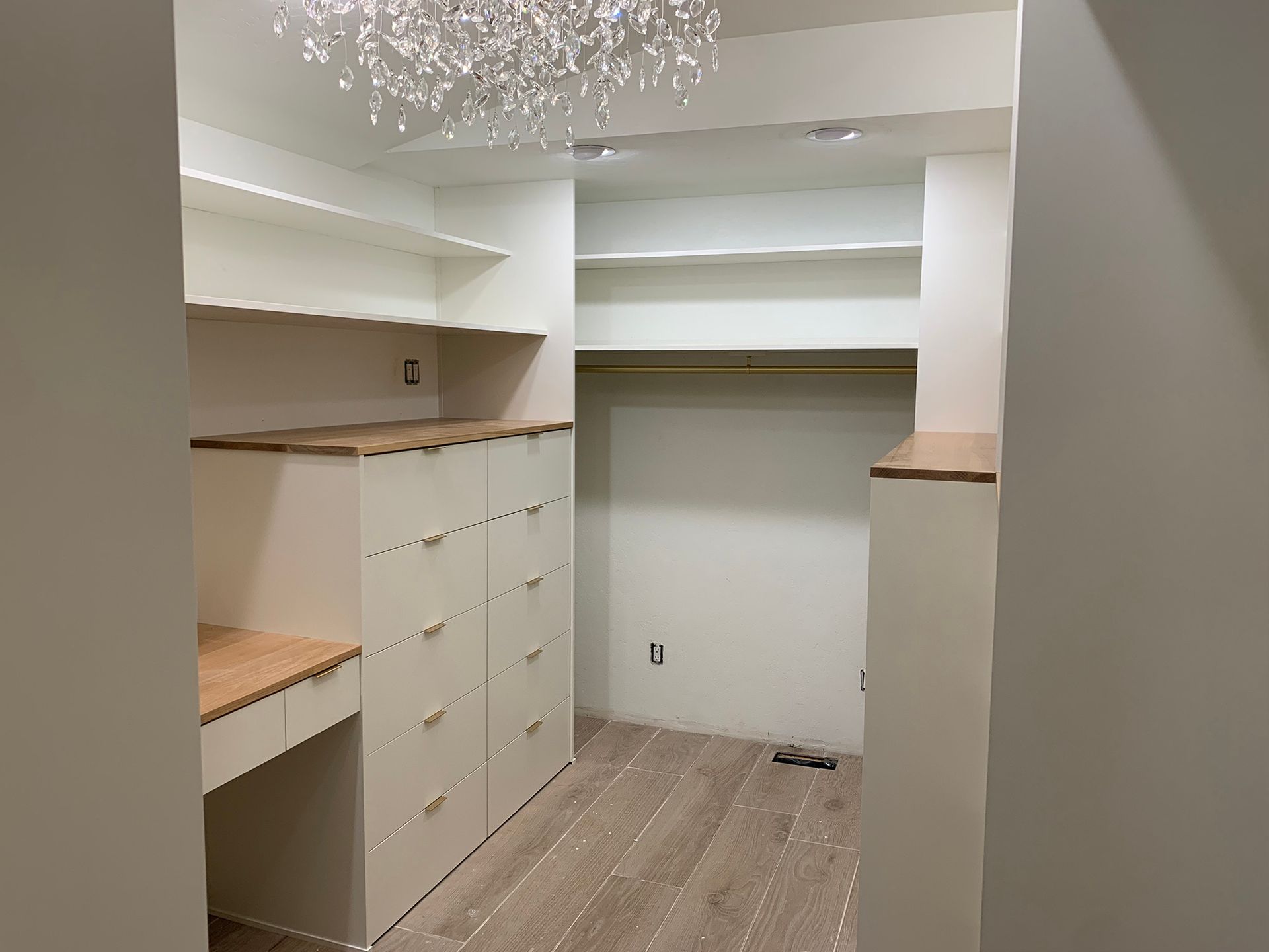 Walk-in closet with white shelves, drawers, and wood countertops under a chandelier