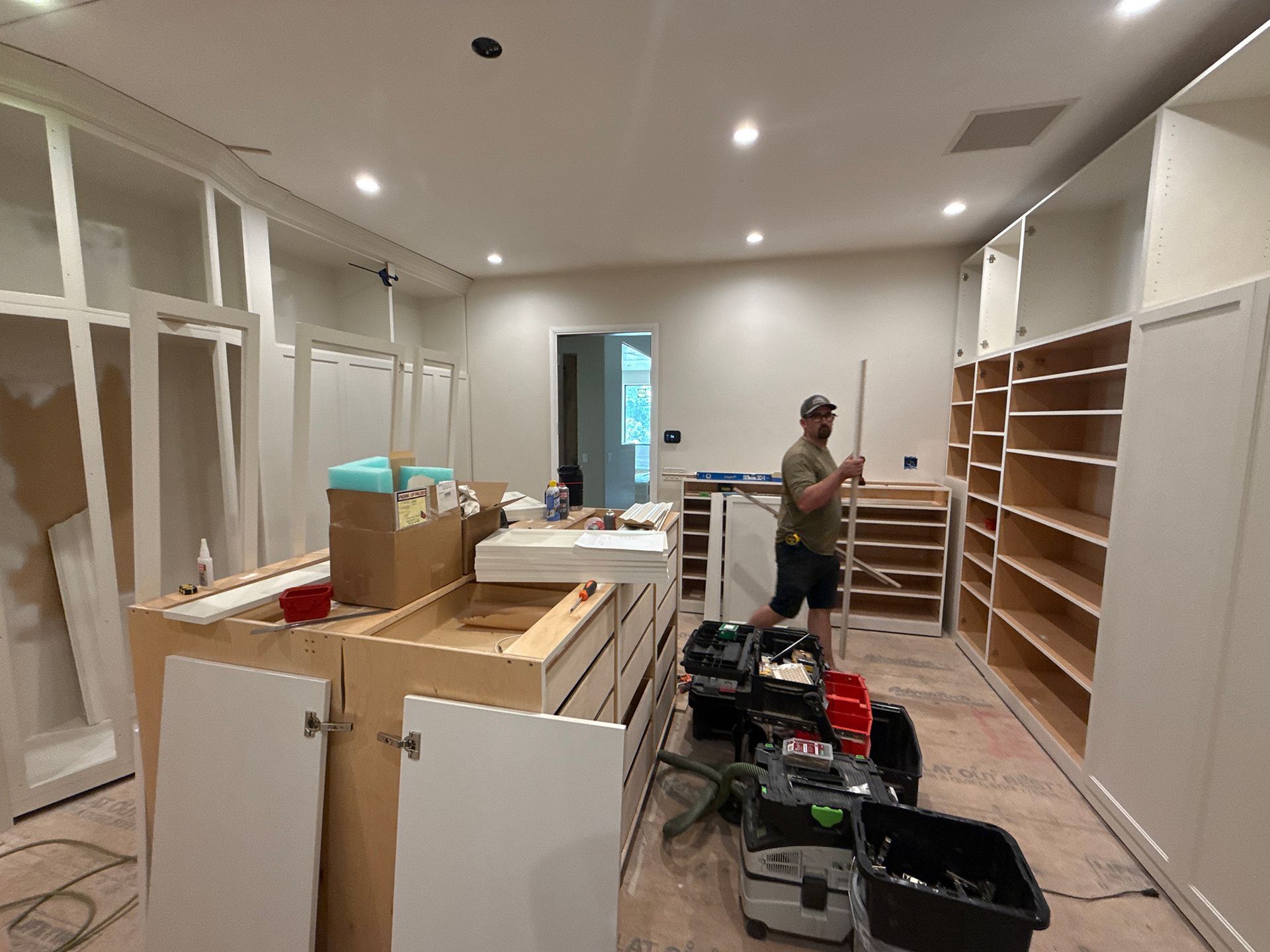 Renovated room with cabinets and shelves; person stands amid tools and boxes during construction.