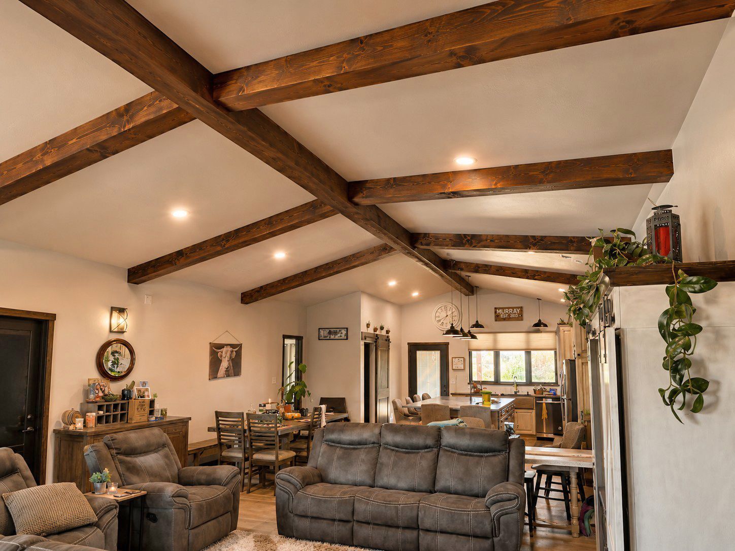 Cozy living room with exposed wood beams, gray sofas, warm lighting, and a dining area in the background
