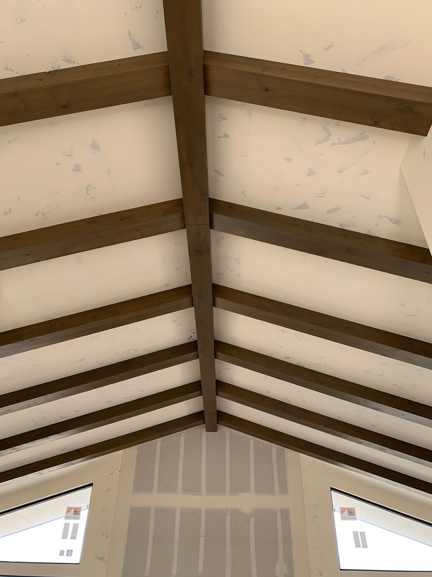 Interior ceiling with exposed dark wooden beams and white panels above a wall