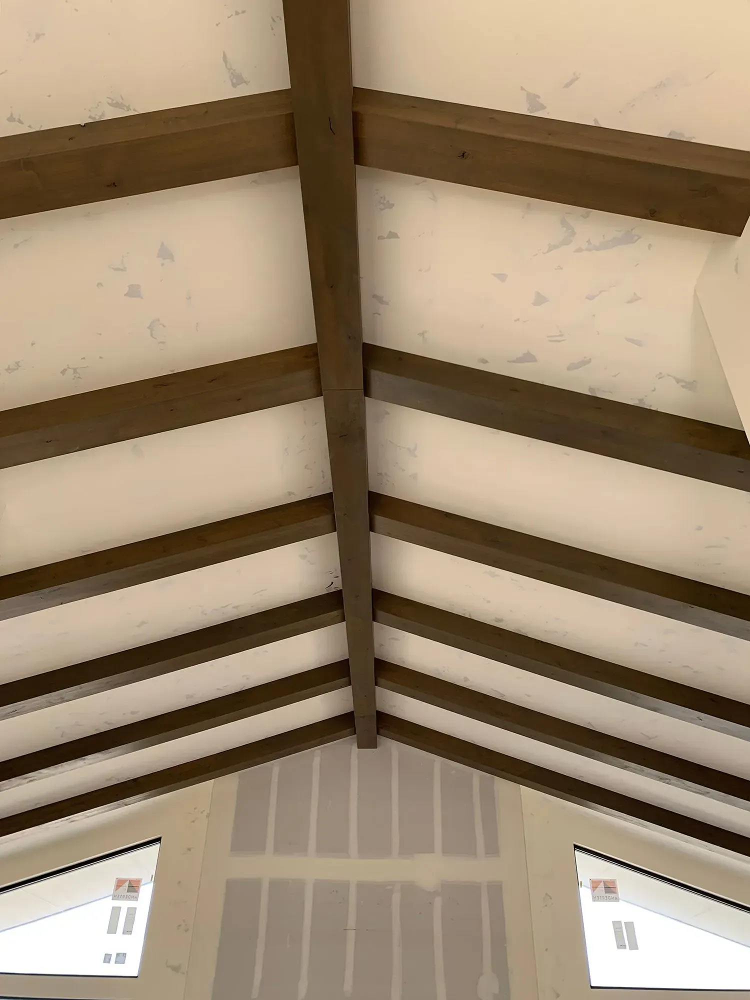 Wooden vaulted ceiling with exposed beams and white panels above a partially finished wall.